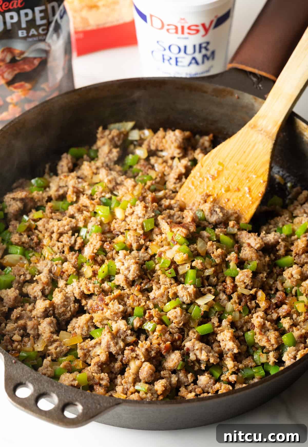 Sausage and vegetables are being expertly cooked in a black pan, destined for a hearty breakfast casserole with hash browns.