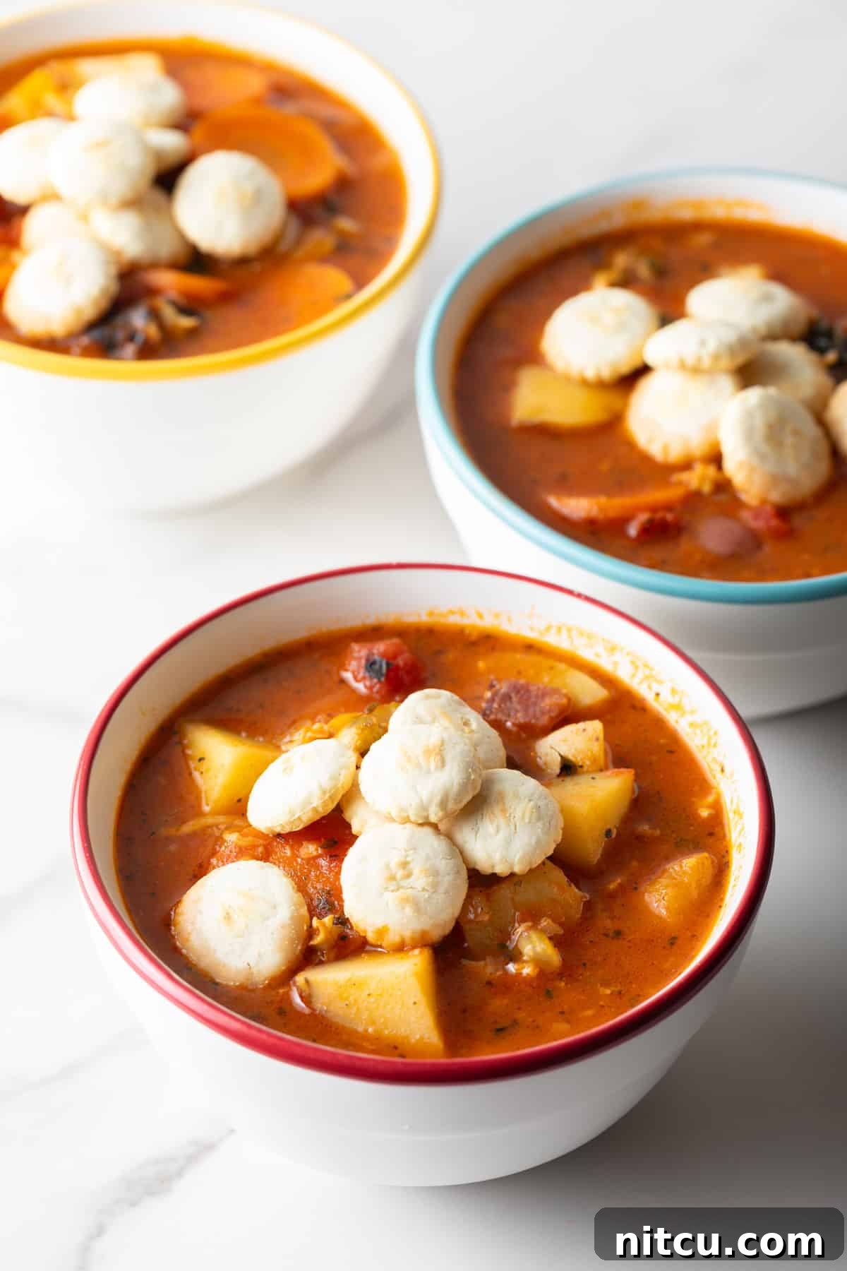 Three white bowls filled with a Manhattan clam chowder recipe topped with oyster crackers.