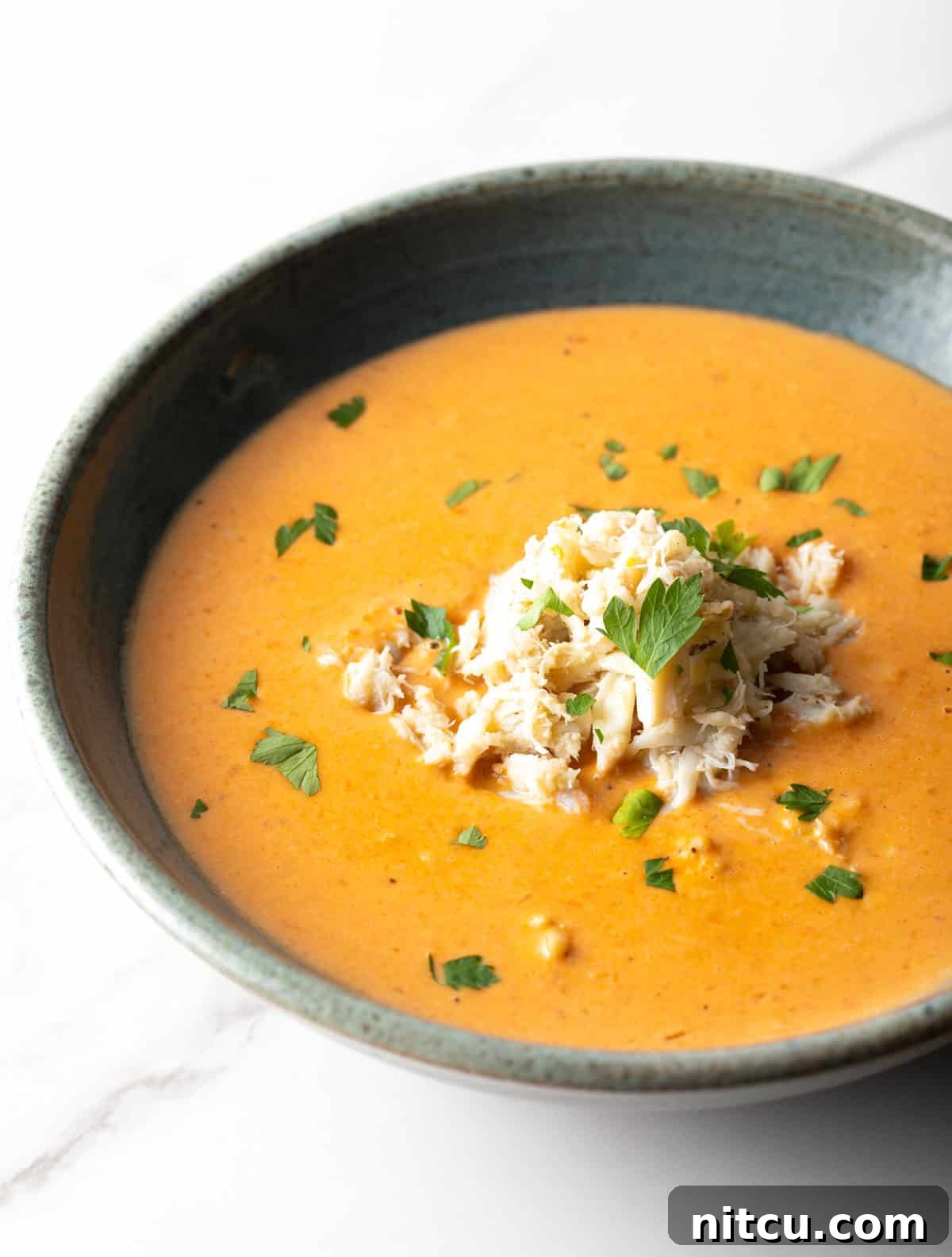 A black bowl filled with creamy crab bisque soup with crab meat and parsley on top.