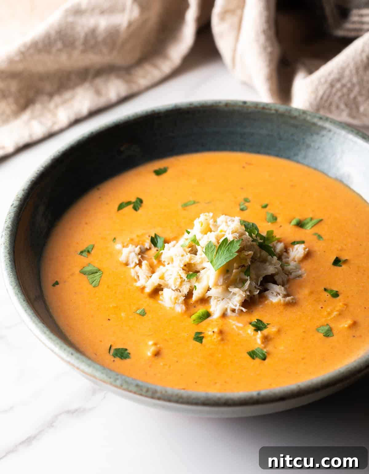 A grey bowl filled with a creamy crab bisque soup recipe, with crab meat and parsley on top.