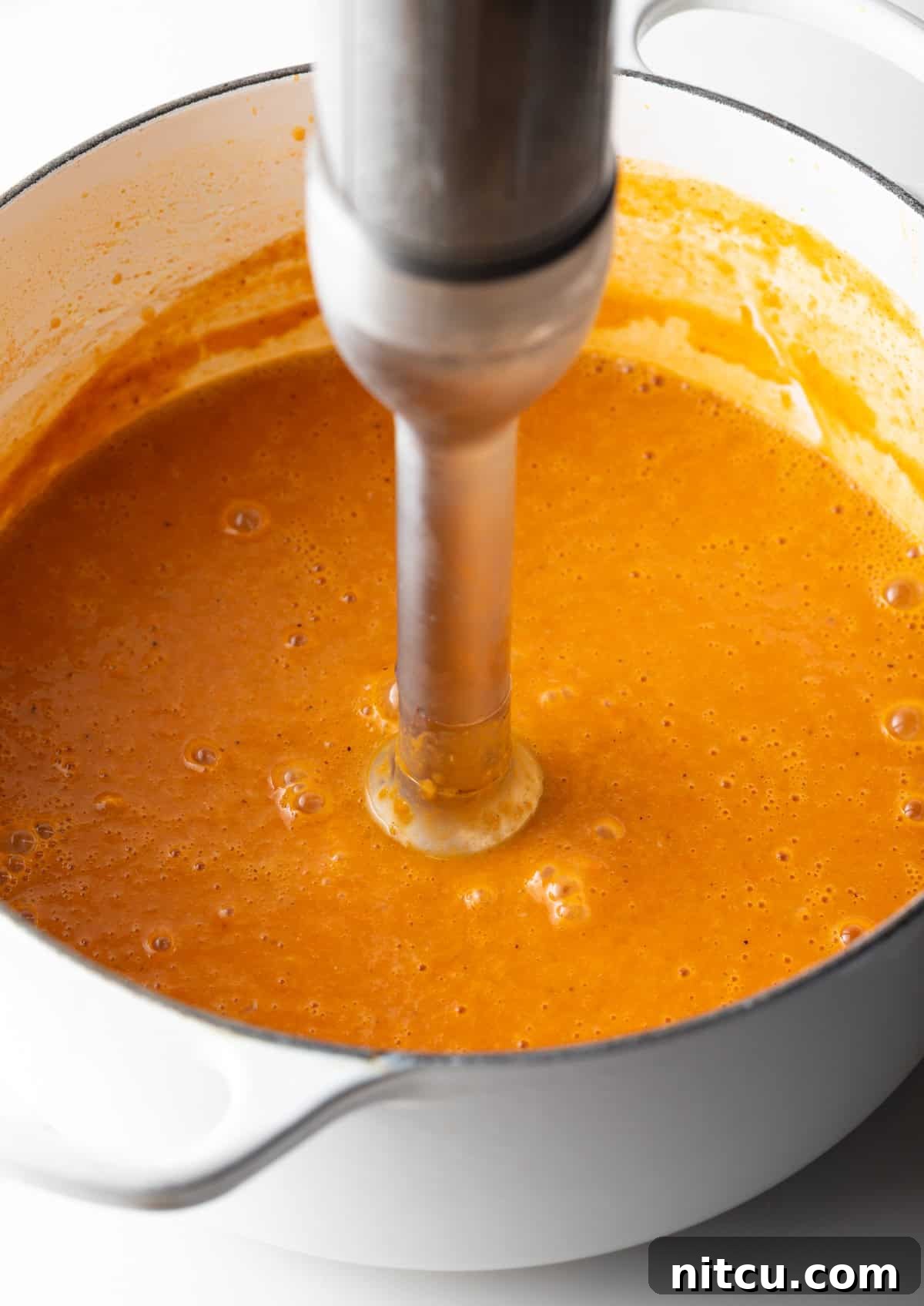 An immersion blender is blending a crab bisque soup base.