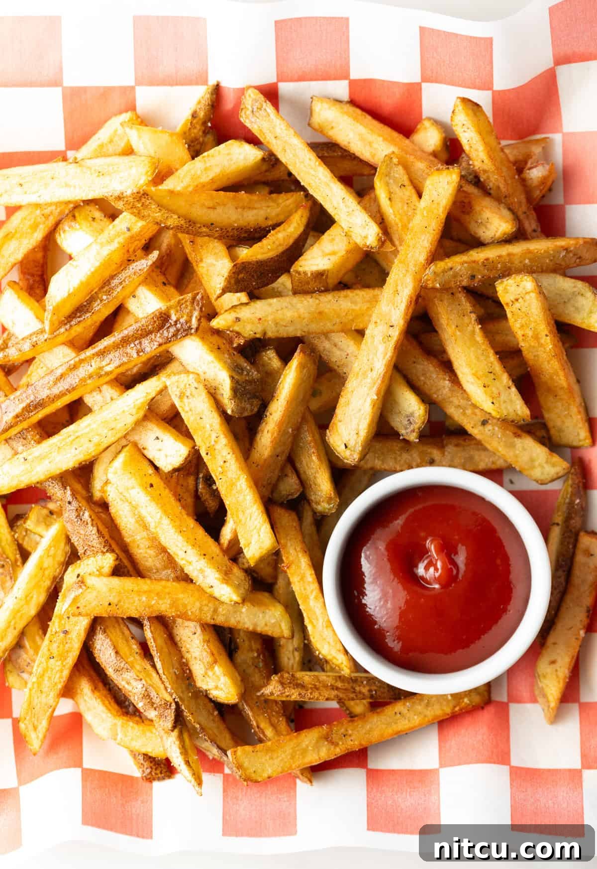 Top down view freshly fried potatoes in a pile with ramekin of ketchup on the side.