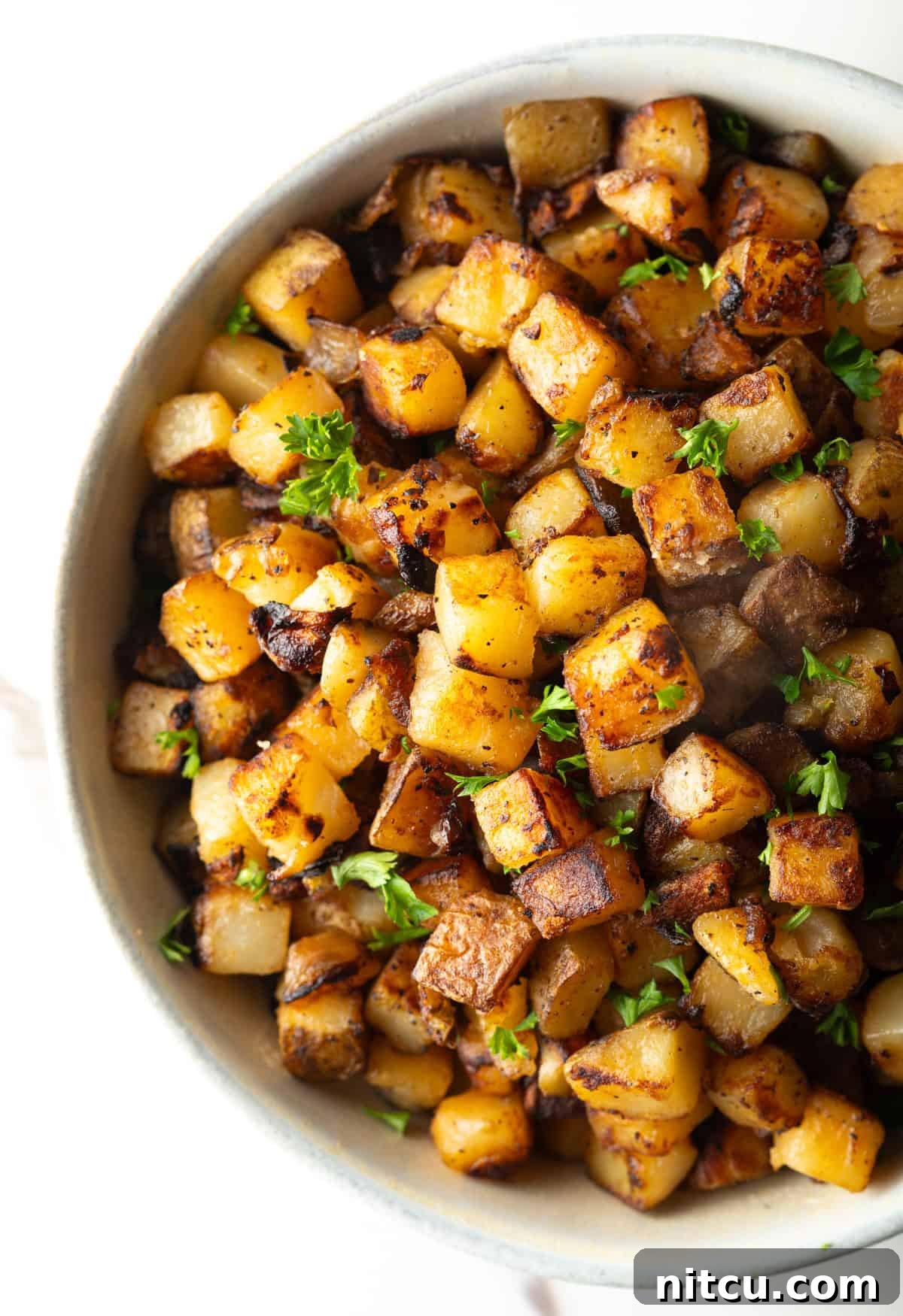 Crispy skillet potatoes garnished with fresh parsley, sitting in a white bowl.
