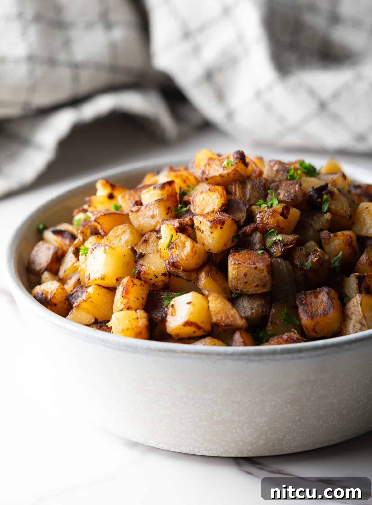 Side view of a white bowl filled with homemade skillet potatoes.