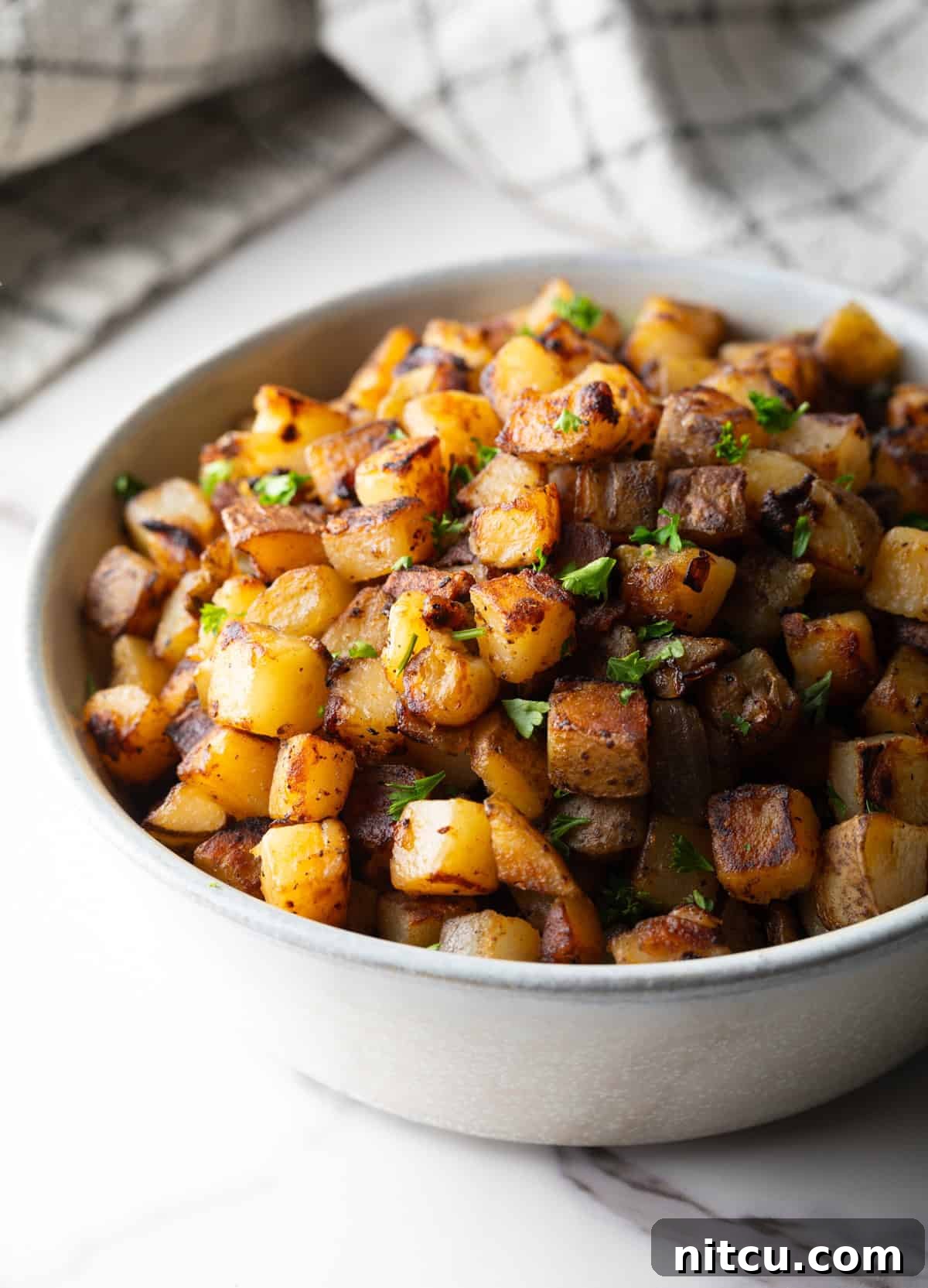 A crispy breakfast home fries recipe topped with fresh parsley, sitting in a white bowl.