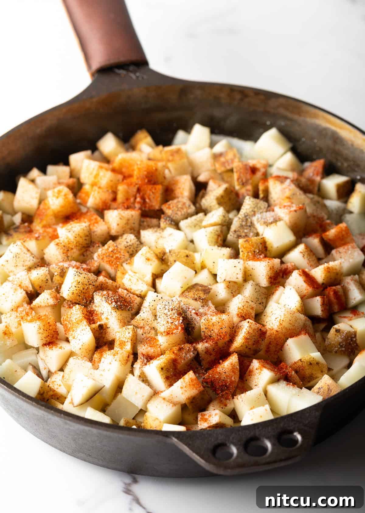 Raw cubed potatoes topped with smoked paprika sitting in a black skillet.