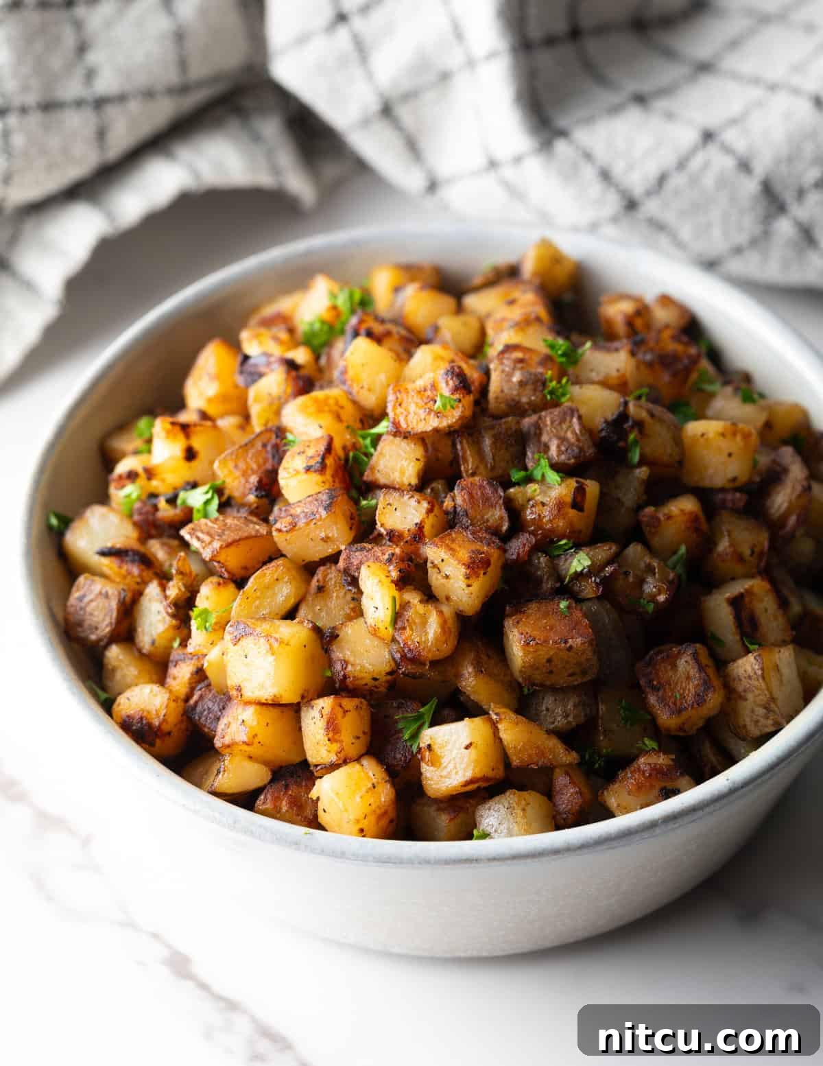 Crispy homefries topped with fresh parsley, sitting in a white bowl ready for serving.