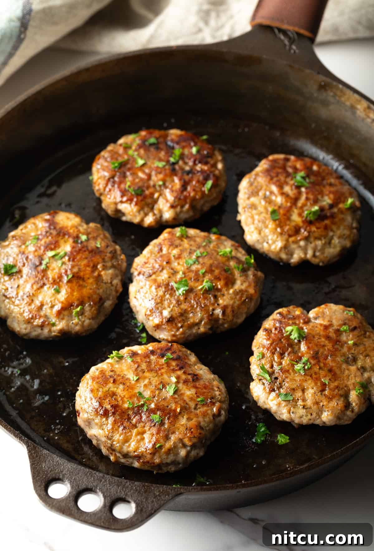 Homemade breakfast sausage patties are being cooked and browned in a black skillet.