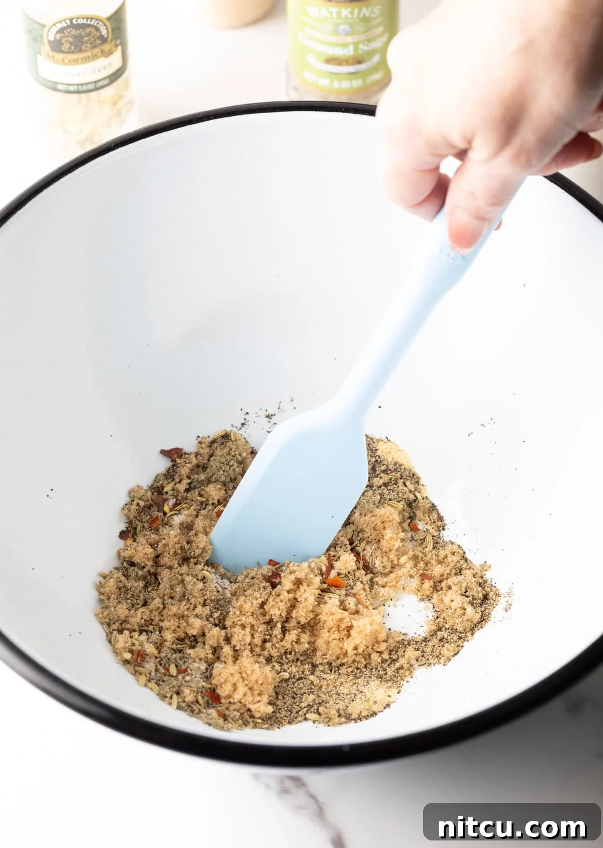 A mix of herbs and spices being stirred in a white bowl with a spatula.