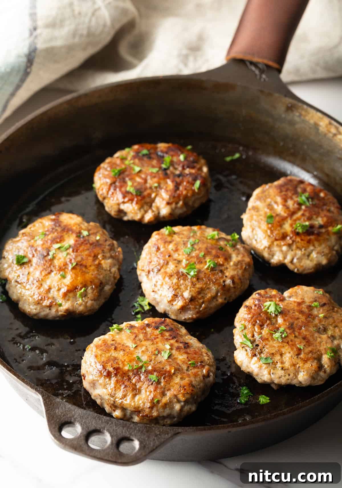 A homemade breakfast sausage recipe is being cooked and browned in a black skillet.