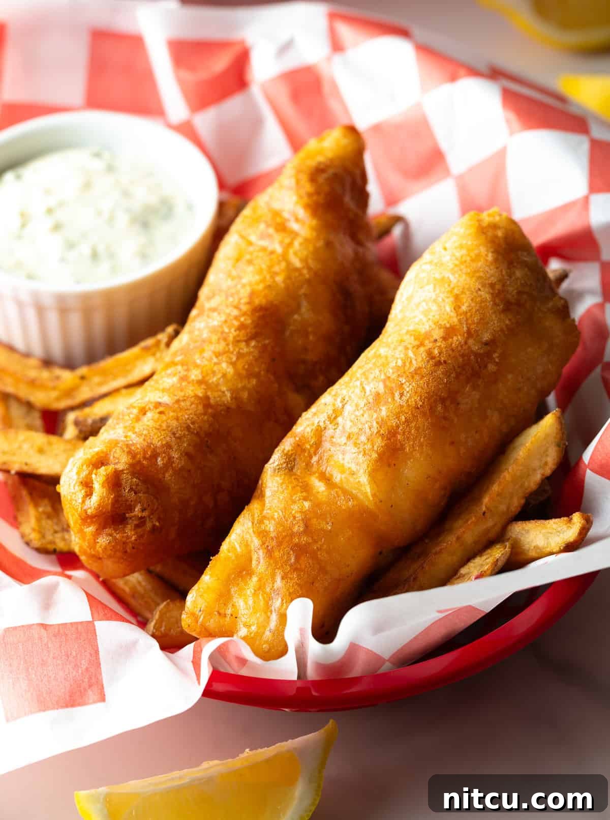 A crispy battered fried fish recipe in a paper lined basket, sitting on top of French fries.