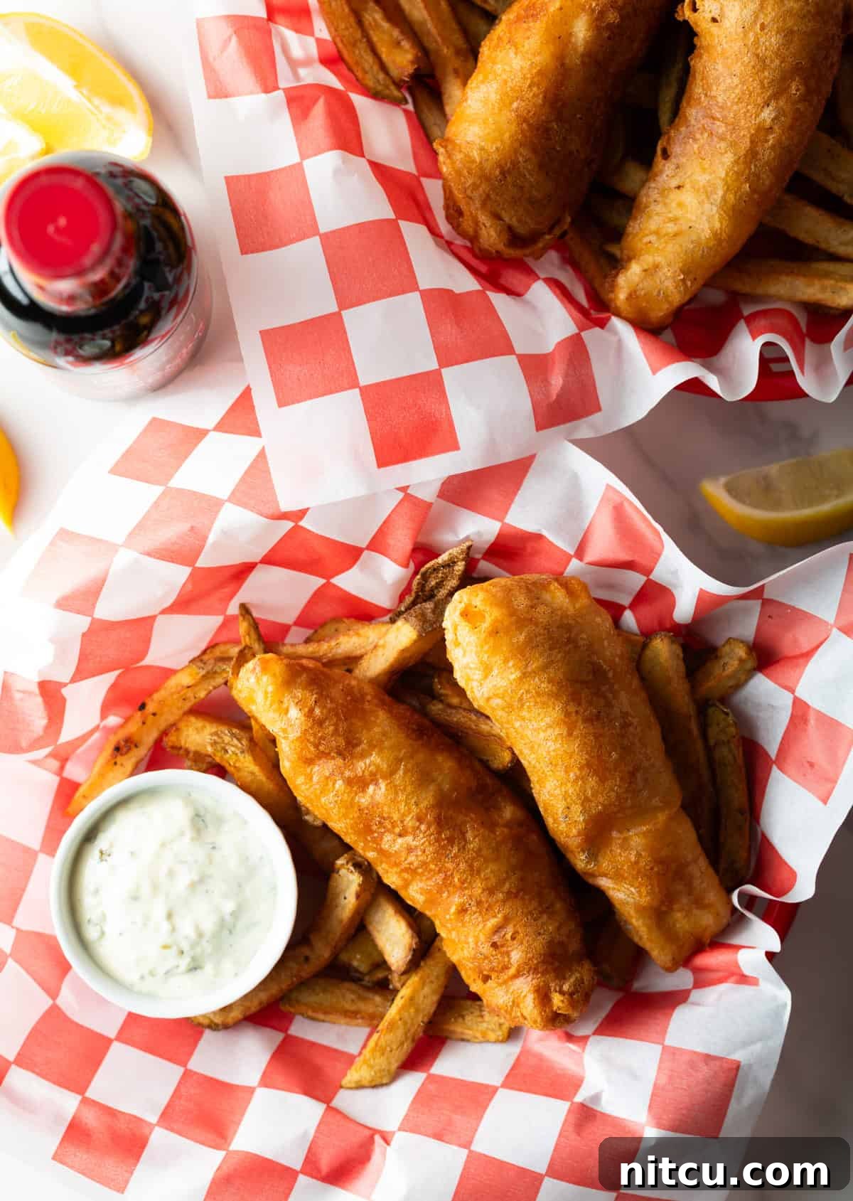 An overhead shot of a fried fish recipe sitting in a basket with French fries and a ramekin of sauce.