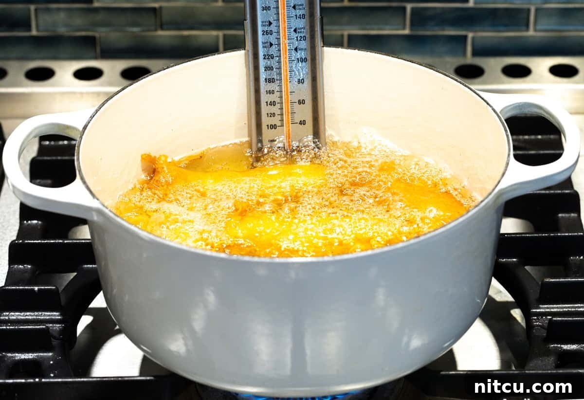 Battered fish filets are frying in a pot filled with oil and a cooking thermometer.