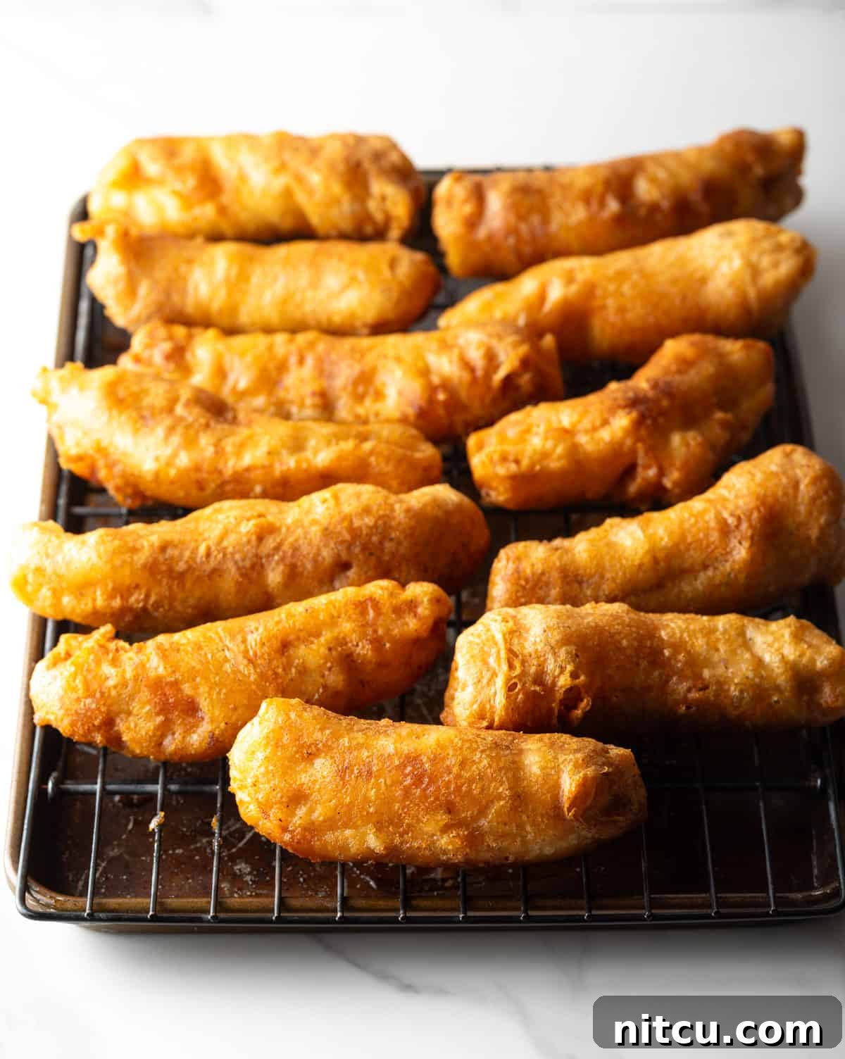 Crispy beer battered fish pieces lined up on a black drying rack.