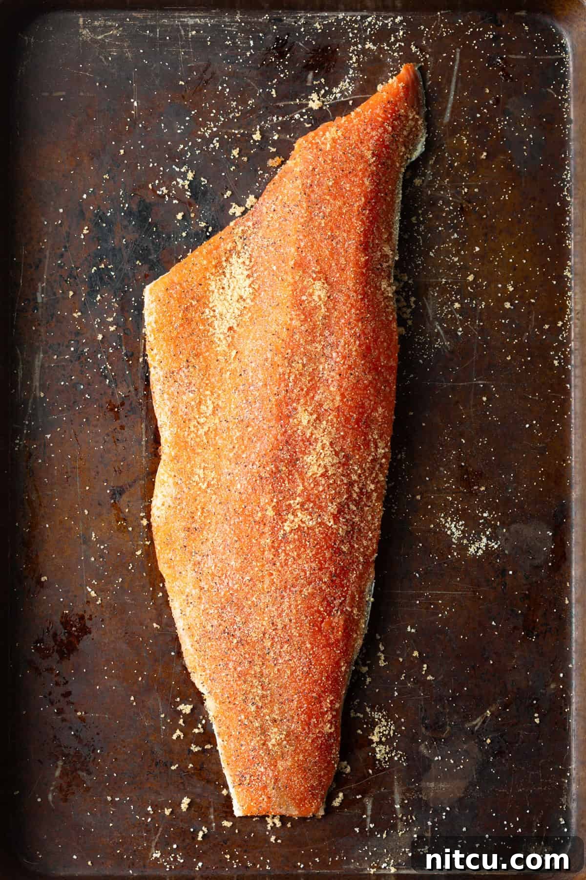 A whole fillet of raw salmon that has been sprinkled with seasoning, sitting on a baking tray.