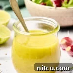 A honey lime dressing recipe in a glass jar with a spoon in it, ready for serving.