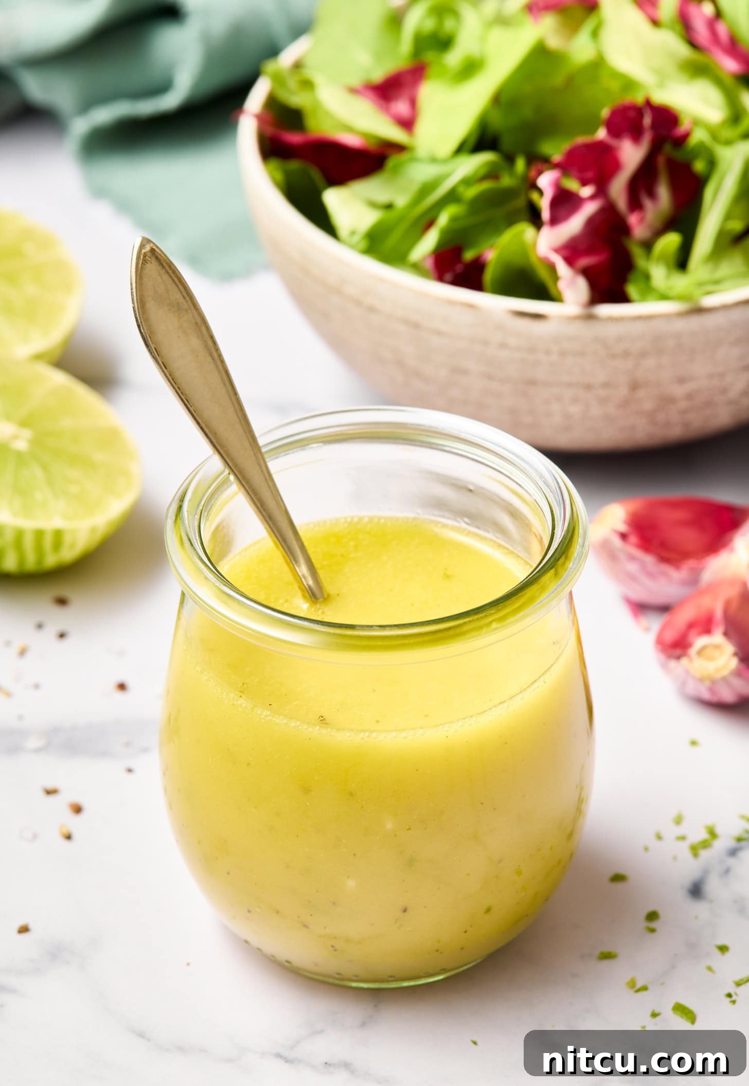 A honey lime vinaigrette recipe in a glass jar with a spoon in it.