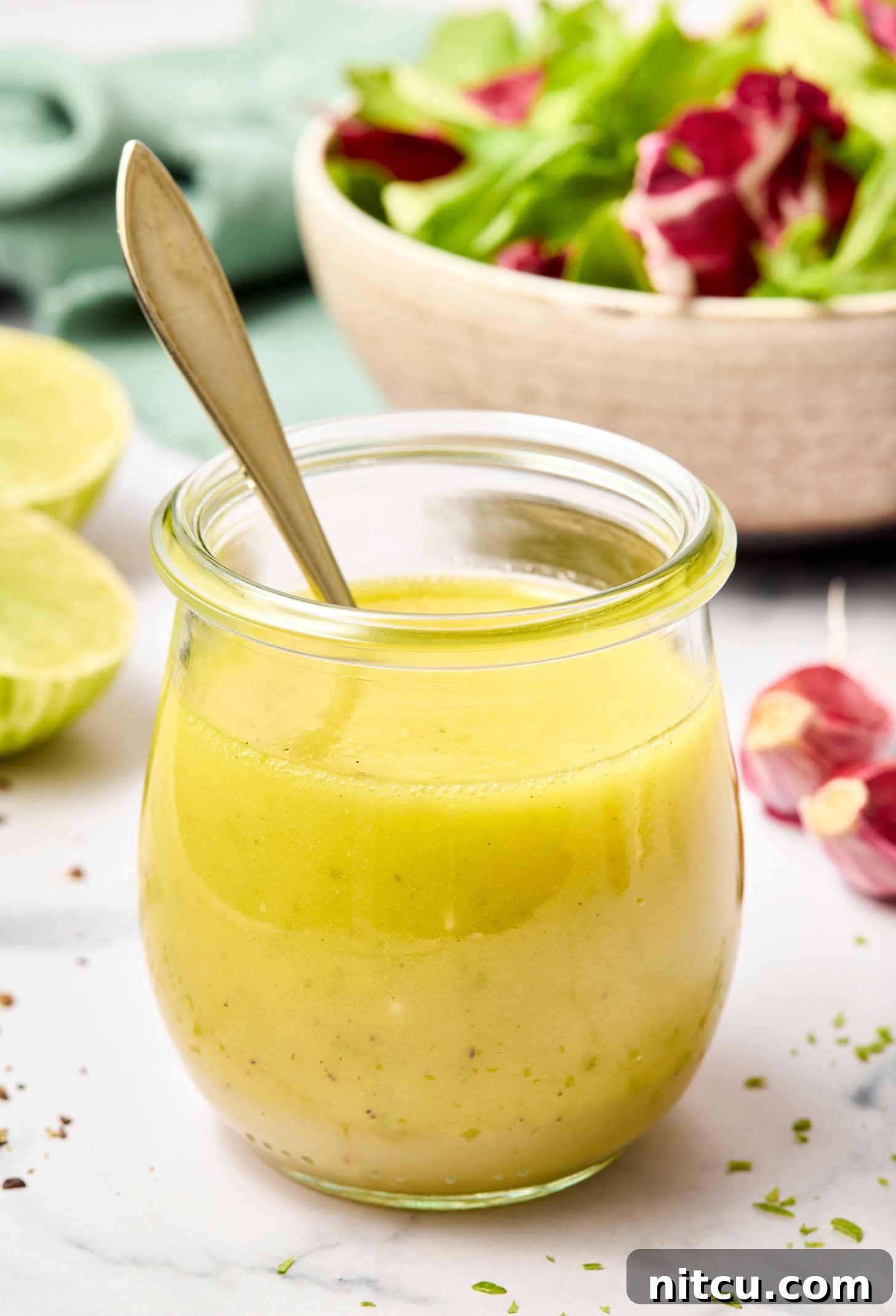 A honey lime dressing recipe in a glass jar with a spoon in it, ready for serving.