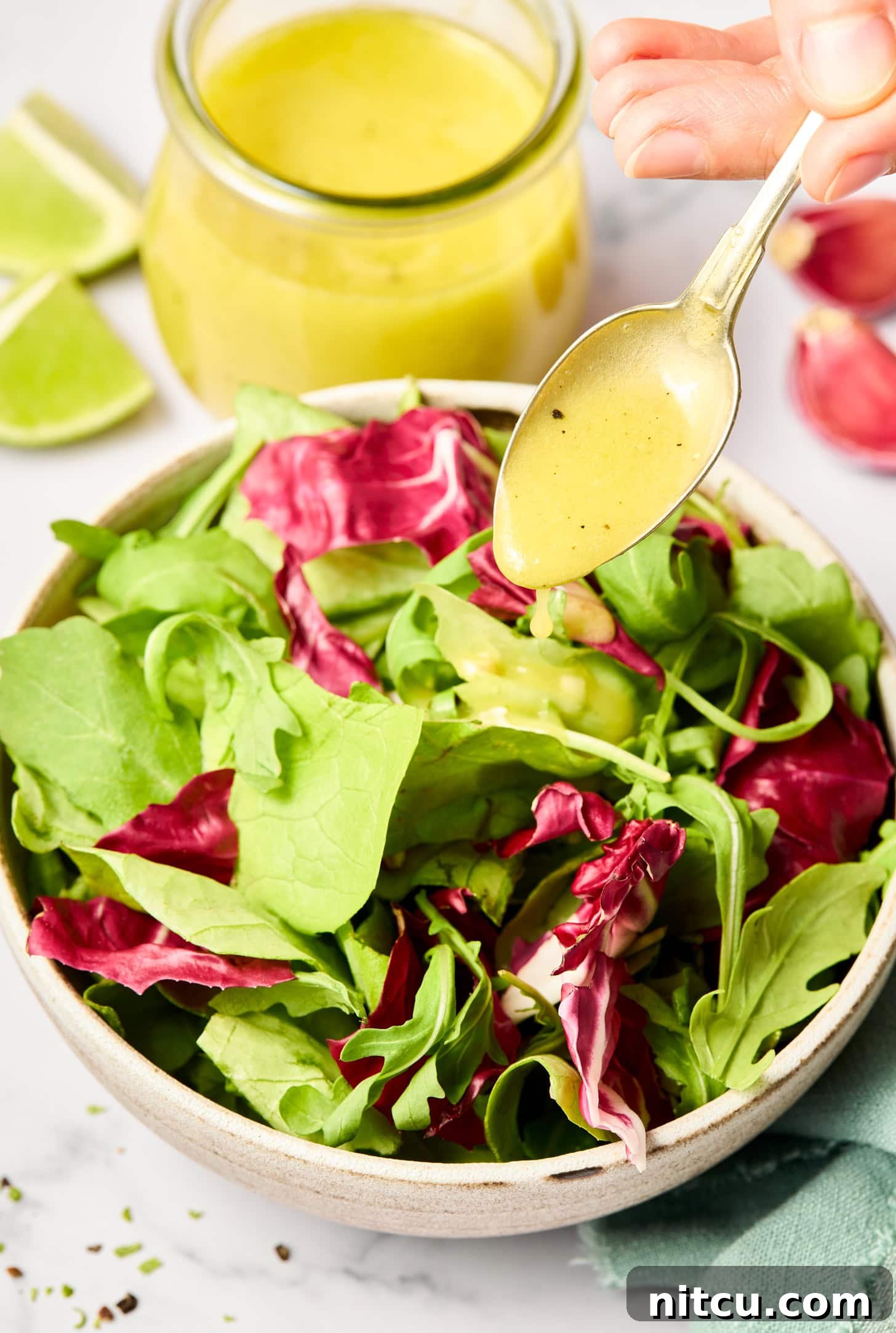 A spoonful of lime vinaigrette is being poured over a fresh greens salad.