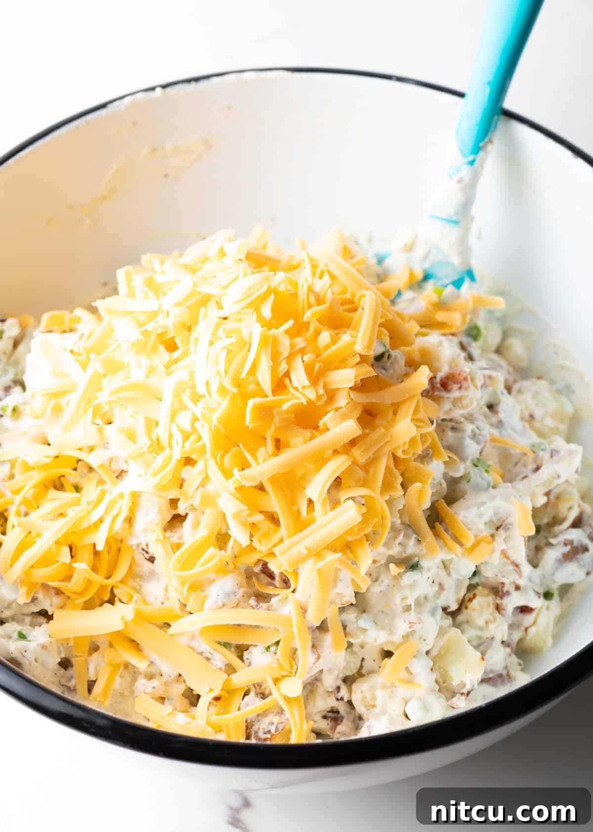 A bowl filled with loaded baked potato salad, topped with shredded cheddar cheese.