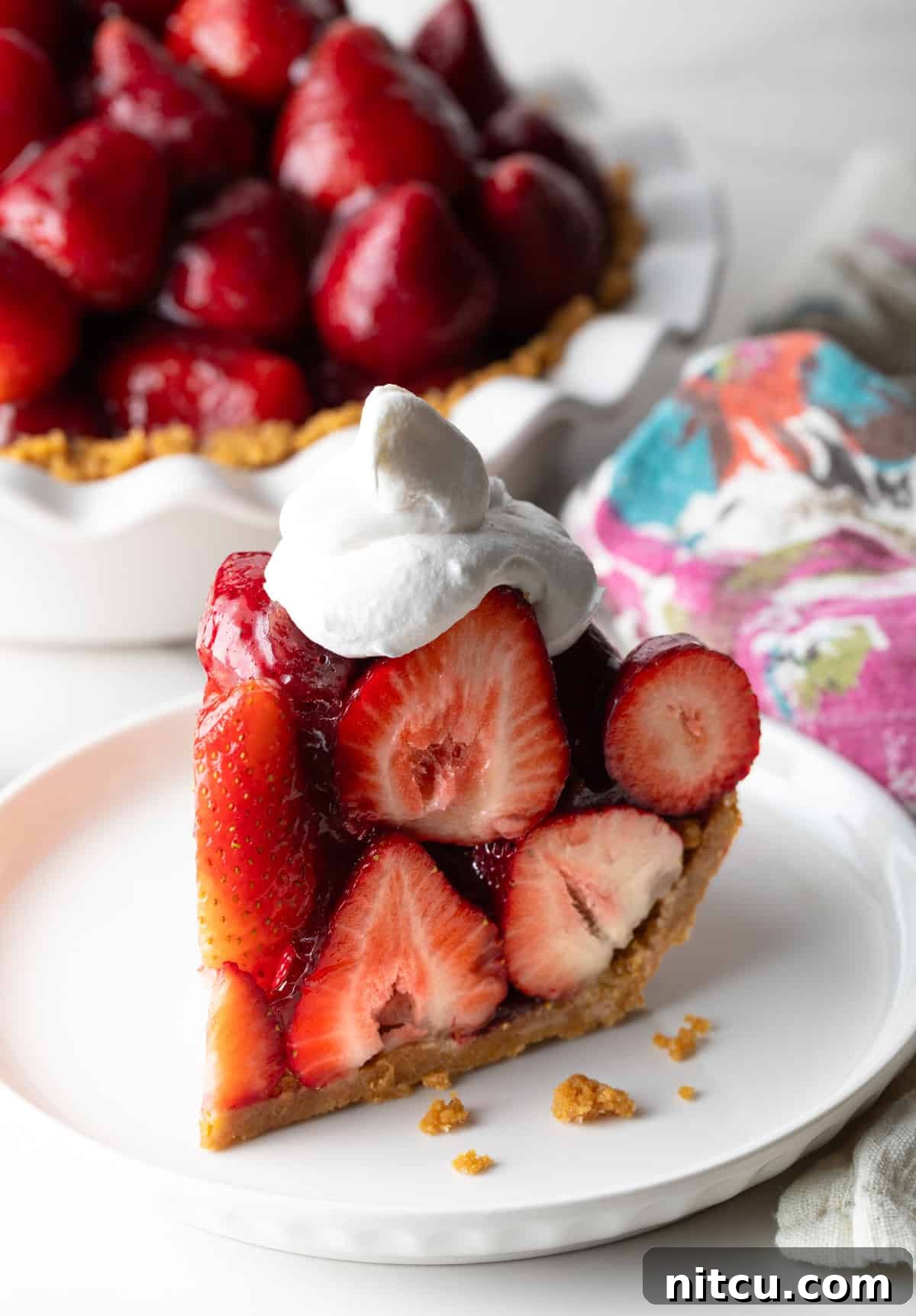 A slice of easy no-bake strawberry pie topped with whipped cream, sitting on a white plate.