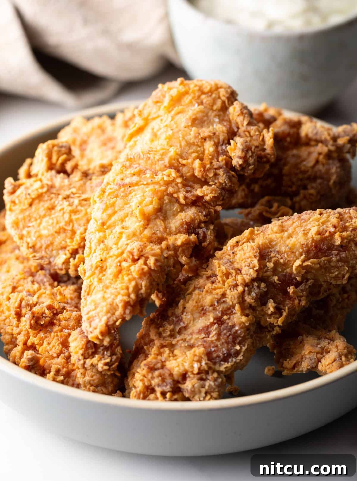 Crispy Deep-Fried Chicken Tenders Recipe That Delivers 2 Crispy deep fried chicken tenders sitting in a white bowl.