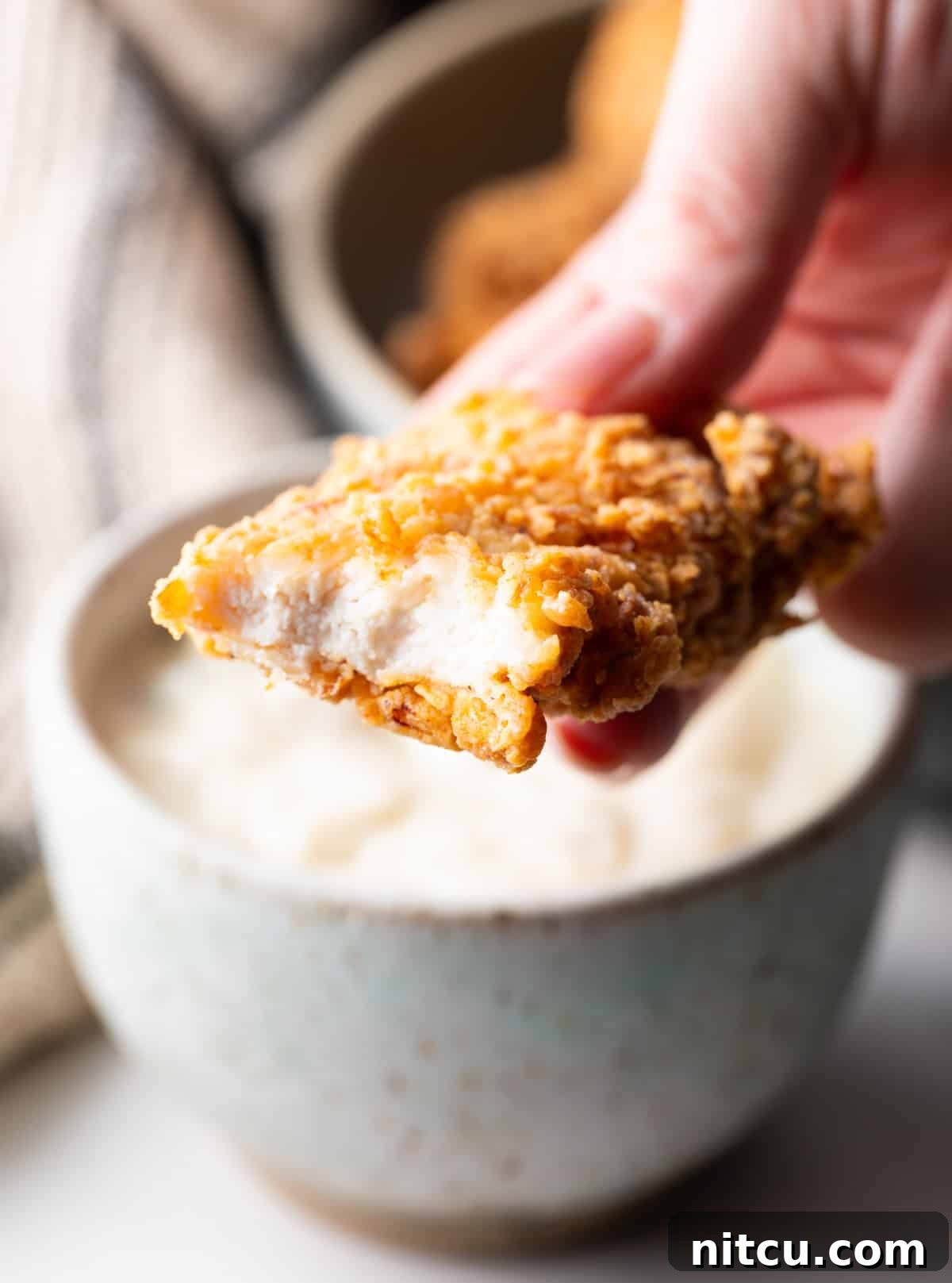 Crispy Deep-Fried Chicken Tenders Recipe That Delivers 5 A hand holding a deep fried chicken tender with a bite taken out.