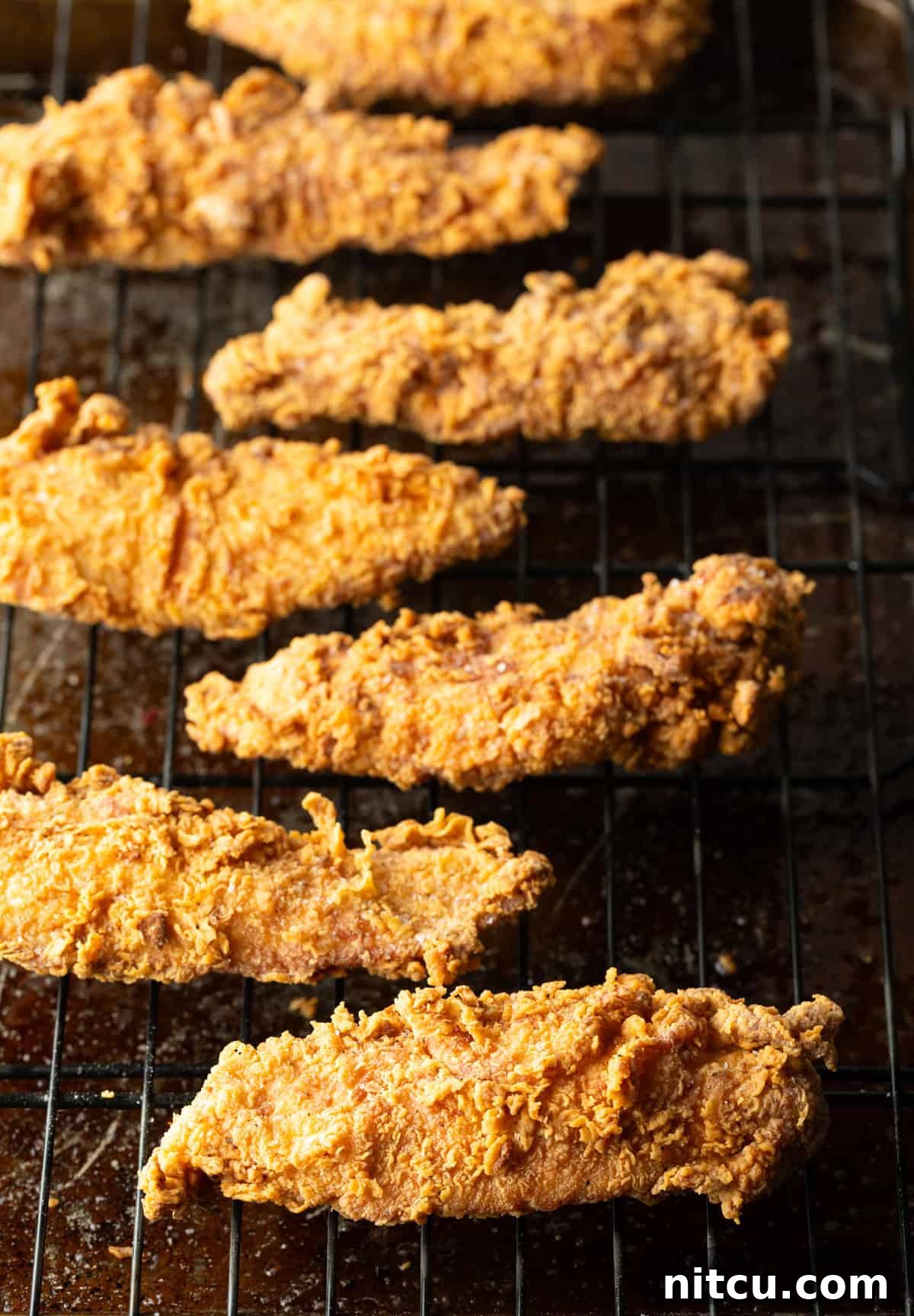 Crispy Deep-Fried Chicken Tenders Recipe That Delivers 7 Crispy pan fried chicken tenders sitting on a metal drying rack.