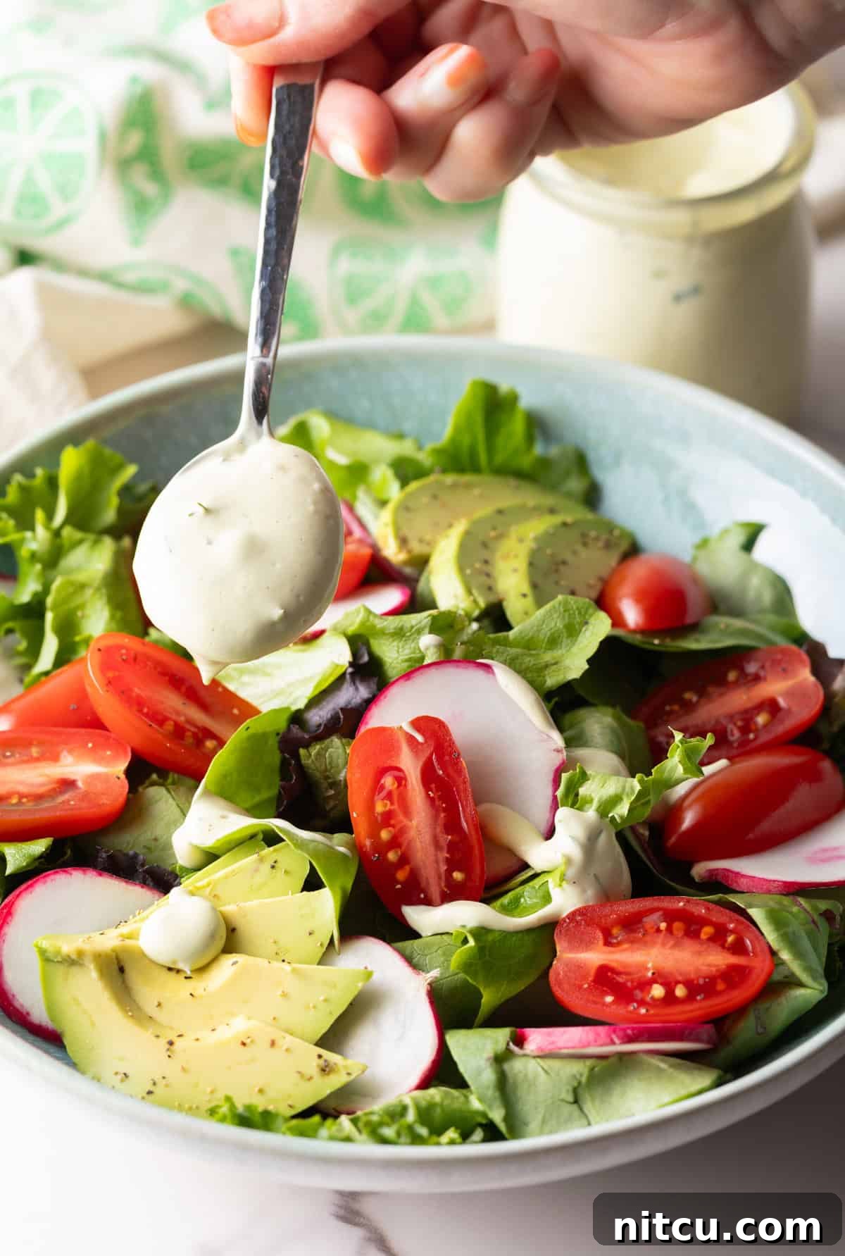 A spoon is drizzling homemade Chick Fil A avocado lime ranch dressing over a salad with tomatoes and avocados.