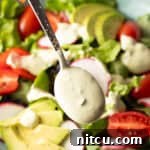 A spoon is drizzling homemade avocado lime ranch dressing over a salad with tomatoes and avocados.