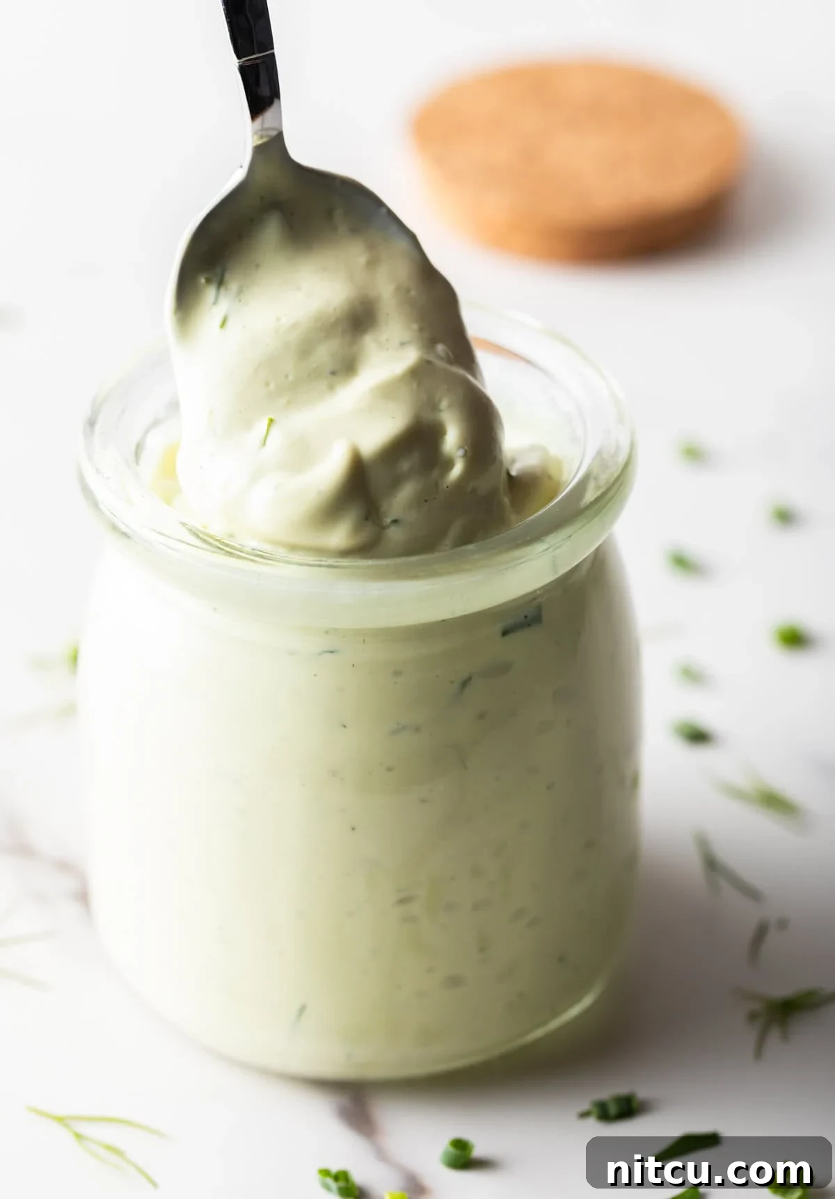 A spoon is scooping a serving of avocado ranch dressing from a glass jar.