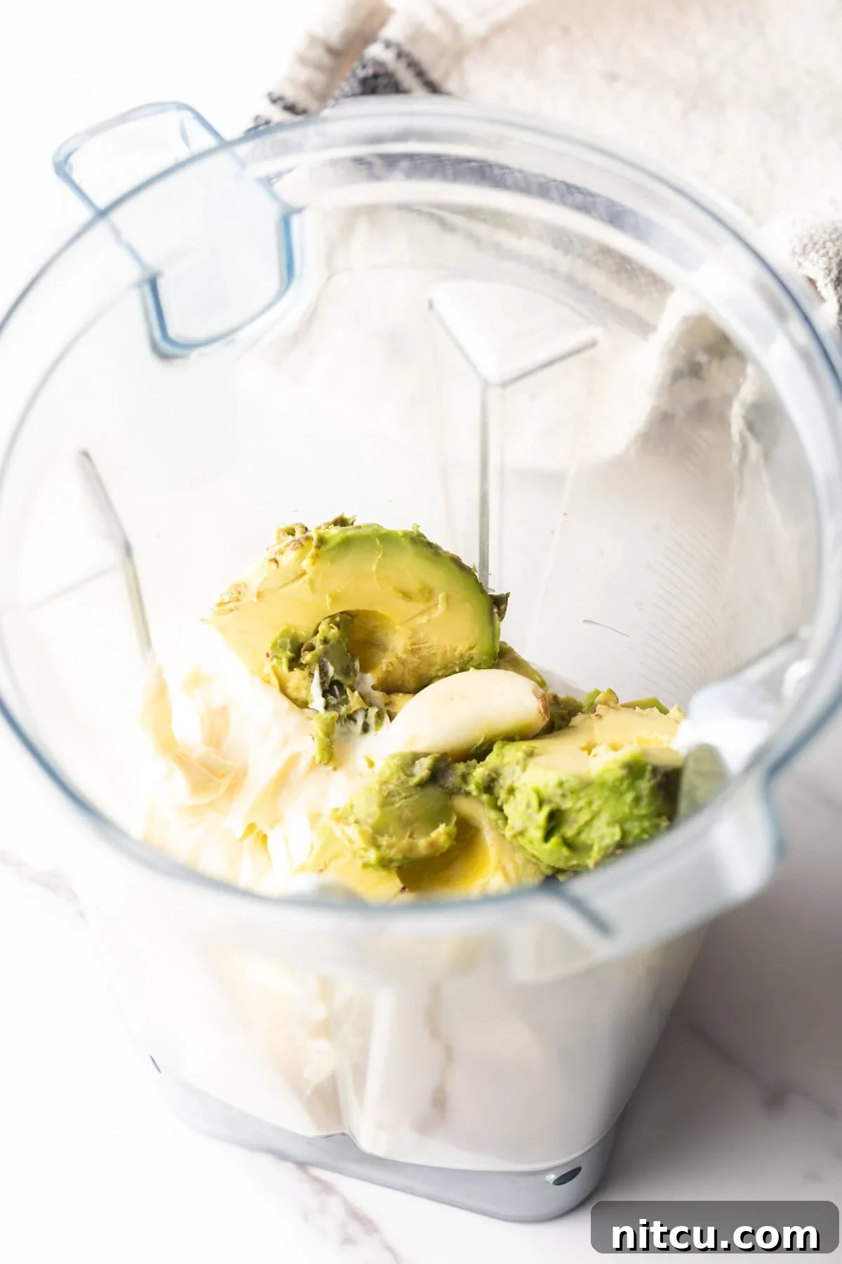Mayonnaise, avocado slices, and lime juice sitting in a blender.