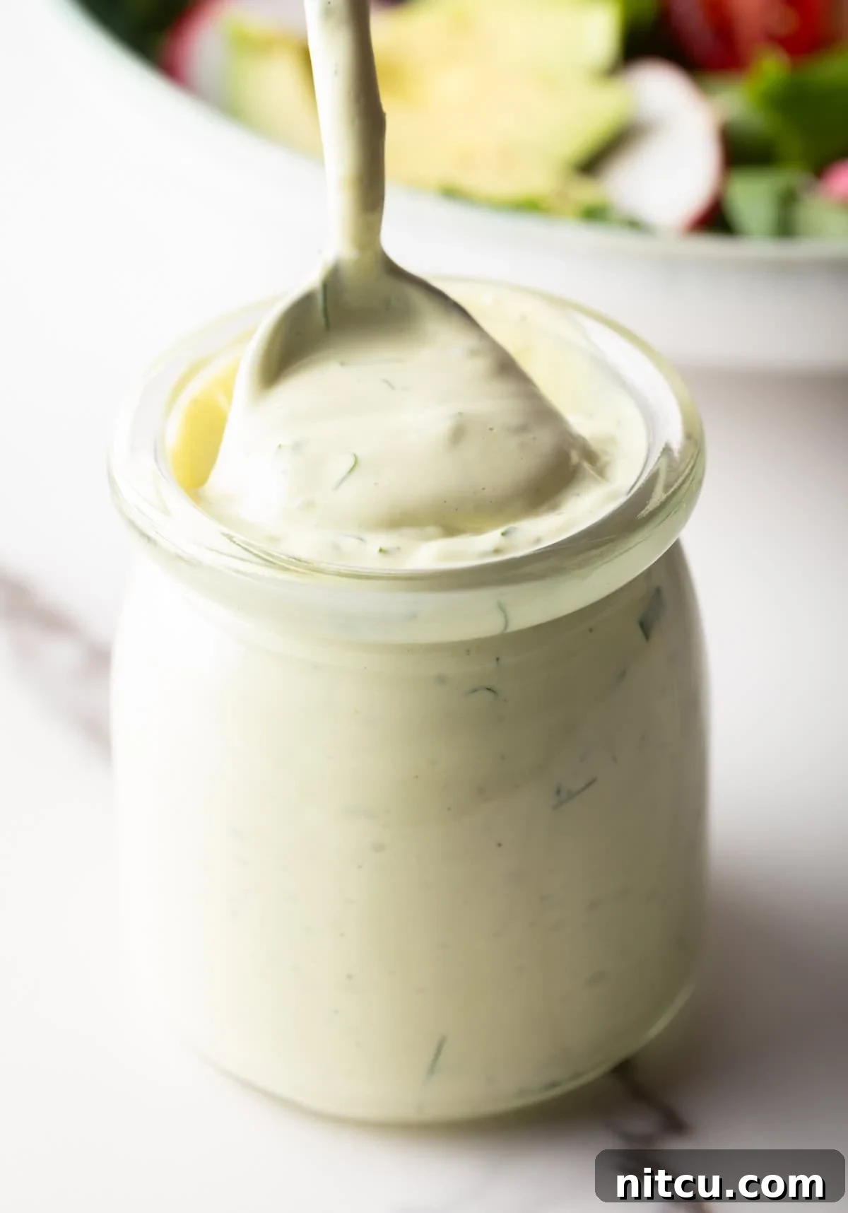 A jar filled with creamy avocado lime ranch dressing, with a spoon scooping a serving.